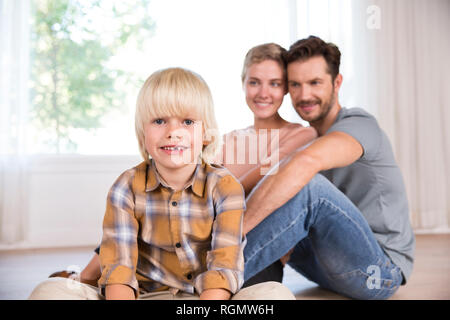 Portrait of smiling boy with parents in background sitting on the floor at home Stock Photo