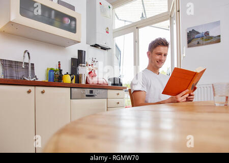 Smiling young man sitting at table at home reading a book Stock Photo