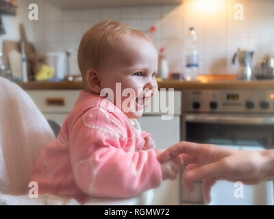 Happy baby girl in sitting in high chair in kitchen