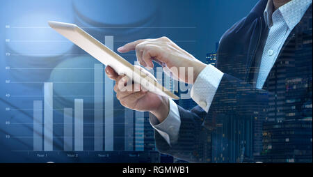 Businessman touching a tablet touch screen reviewing business performance, return on investment - ROI, with cityscape background. Stock Photo