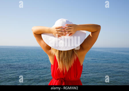 Blond woman in the red dress with the white hat at the beach in Cyprus. Stock Photo
