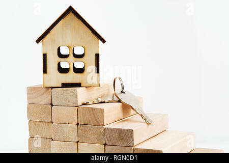 Toy wooden house over wooden stairs with keys, realty concept with light background Stock Photo