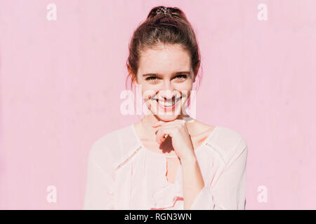 Portrait of smiling young woman in front of pink wall Stock Photo