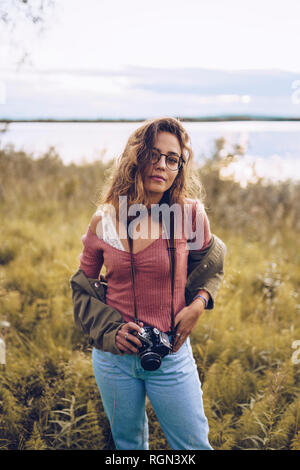 Young woman with camera standing at lake shore Stock Photo