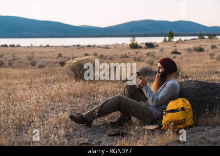 USA, North California, bearded young man using cell phone during a break on a hiking trip near Lassen Volcanic National Park Stock Photo