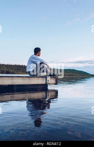 Young man sitting at lake Inari, looking at view, Finland