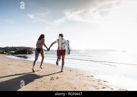 France, Brittany, young couple with surfboard running hand in hand in the sea Stock Photo