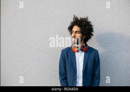 Smiling young businessman with headphones at a wall Stock Photo