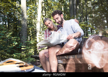 Young couple with map and canoe sitting on a jetty at a forest brook Stock Photo