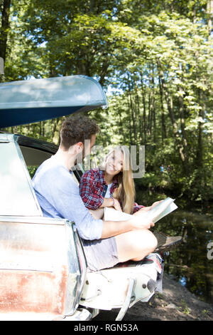 Smiling young couple with map and canoe in car at a brook Stock Photo