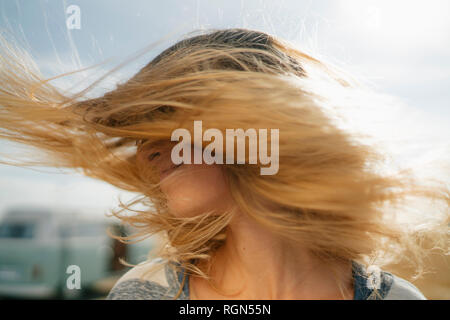 Blong young woman at camper van shaking her hair