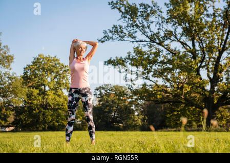 Senior woman stretching on rural meadow Stock Photo
