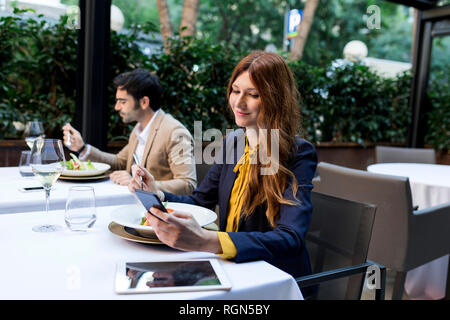 Man eating and woman using cell phone in a restaurant Stock Photo