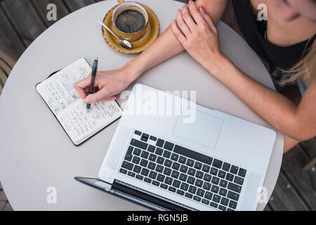 Young woman sitting on balcony with laptop taking notes, top view Stock Photo