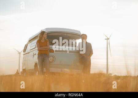 Happy couple at camper van in rural landscape with wind turbines in background Stock Photo
