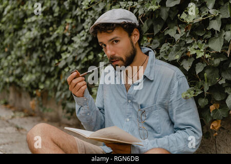 Young man smoking pipe, reading a book Stock Photo