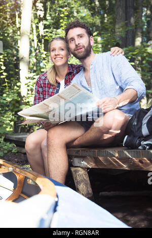 Young couple with map and canoe sitting on a jetty at a forest brook Stock Photo