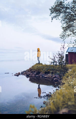 Sweden, Lapland, man wearing  windbreaker standing at water's edge looking at distance Stock Photo
