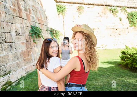 Spain, Mallorca, Palma, two female friends smiling at camera while another friend is taking a picture of them Stock Photo