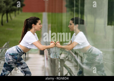 Young woman doing stretching exercise reflected in glass facade Stock Photo