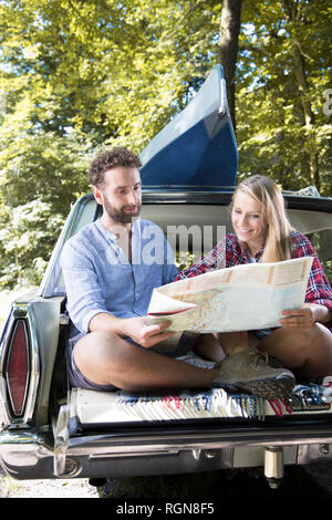 Smiling young couple with map and canoe in car at a brook Stock Photo