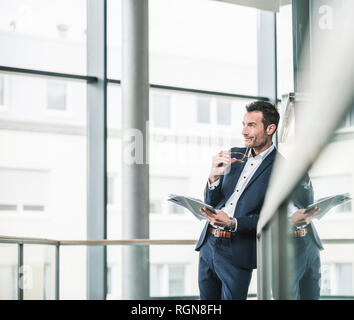 Businessman standing in office building, using digital tablet Stock Photo