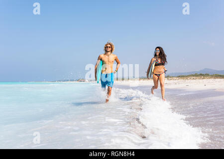 Couple running on the beach, carrying surfboards Stock Photo