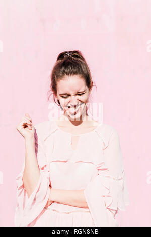 Portrait of young woman grimacing in front of pink wall Stock Photo