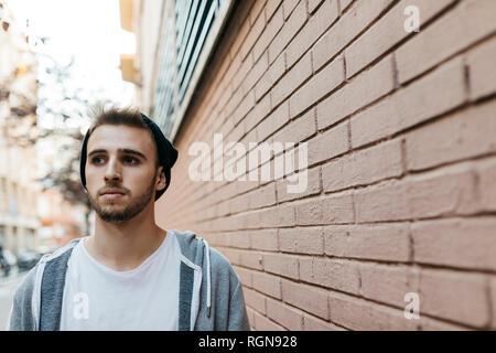 Young man walking in the city next to a wall