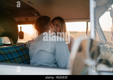 Young couple kissing in camper van at sunset Stock Photo