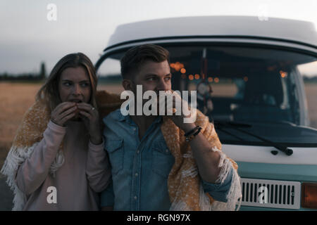 Couple wrapped in a blanket at camper van having a snack in rural landscape Stock Photo
