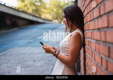 Young woman in front of a brick wall using smartphone Stock Photo