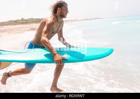 Young man running into ghe sea, carrying his surfboard Stock Photo
