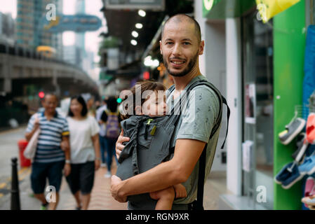 China, Hong Kong, portrait of father travelling with a little girl sleeping in a baby carrier Stock Photo