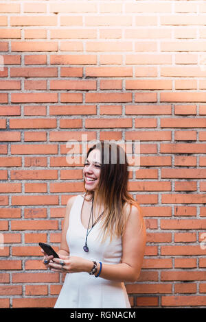 Laughing young woman in front of a brick wall using smartphone Stock Photo