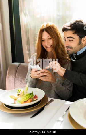 Happy couple using cell phone in a restaurant Stock Photo