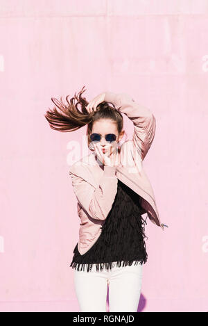 Portrait of young woman wearing sunglasses posing in front of pink wall Stock Photo