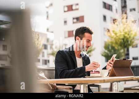 Businessman sitting in cafe, drinking coffee, using smartphone Stock Photo