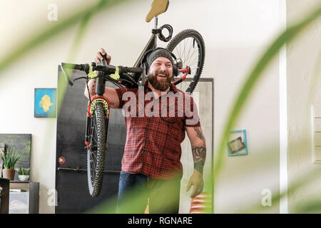 Laughing man wearing headphones carrying bicycle in office Stock Photo
