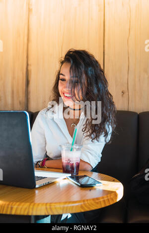 Portrait of smiling young woman in a coffee shop using laptop Stock Photo