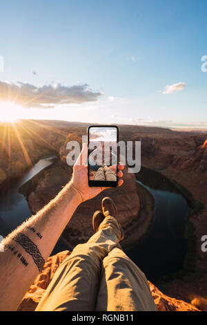 USA, Arizona, Colorado River, Horseshoe Bend, young man on viewpoint, holding smartphone Stock Photo