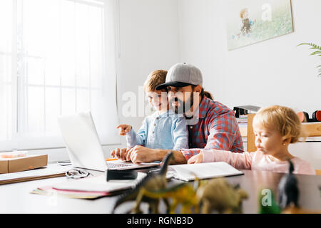 Father working at home, using laptop with his children on his lap Stock Photo