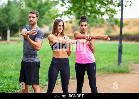 Young athletes doing shoulder stretches in a park Stock Photo