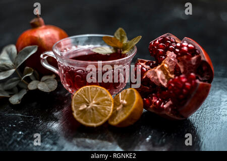Close up of herbal and organic tea of pomegranate on wooden surface in transparent cup with raw pomegranate and sliced lemons with sugar. Stock Photo