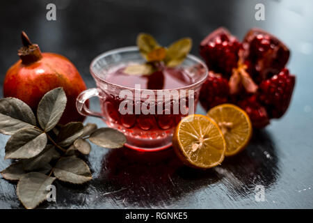 Close up of herbal and organic tea of pomegranate on wooden surface in transparent cup with raw pomegranate and sliced lemons with sugar. Stock Photo