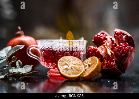 Close up of herbal and organic tea of pomegranate on wooden surface in transparent cup with raw pomegranate and sliced lemons with sugar. Stock Photo