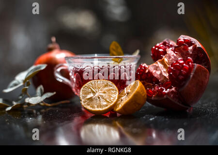 Close up of herbal and organic tea of pomegranate on wooden surface in transparent cup with raw pomegranate and sliced lemons with sugar. Stock Photo