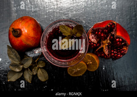 Close up of herbal and organic tea of pomegranate on wooden surface in transparent cup with raw pomegranate and sliced lemons with sugar. Stock Photo