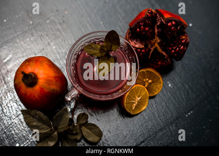 Close up of herbal and organic tea of pomegranate on wooden surface in transparent cup with raw pomegranate and sliced lemons with sugar. Stock Photo
