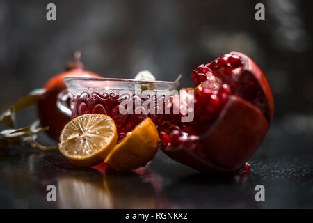 Close up of herbal and organic tea of pomegranate on wooden surface in transparent cup with raw pomegranate and sliced lemons with sugar. Stock Photo